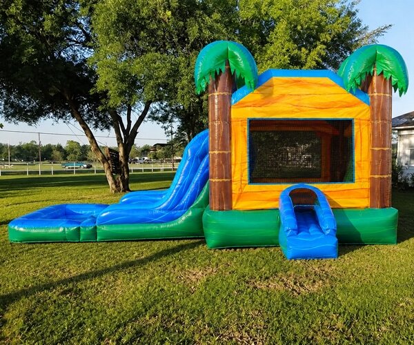 Green and orange palm-tree combo bouncer with an attached blue water slide and splash pool, set up on grass